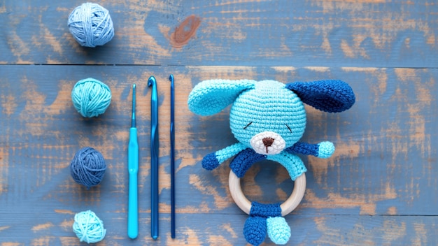 Knitted blue toy for kids with knitting equipment on the table