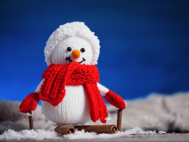 Knitted cheerful snowman in a hat and mittens on a blue background Copy space