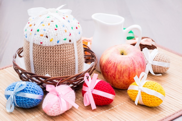 Knitted Easter eggs and cake in a basket and jug on a wooden table