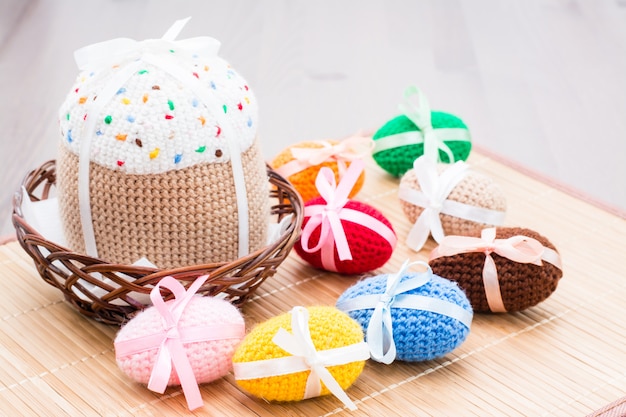 Knitted Easter eggs and Easter cake in a wicker basket on a wooden table