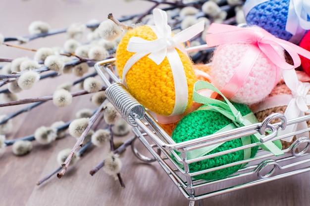 Knitted Easter eggs tied with colored ribbons in a metal basket and willow on a wooden table 