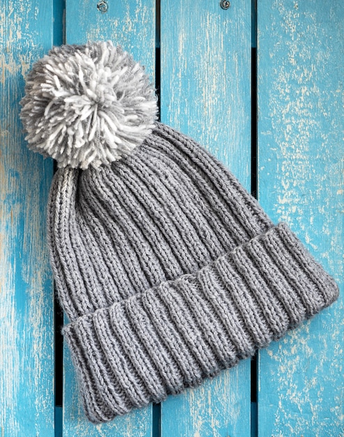 Knitted gray hat with an elastic band two by two with a lapel and a pompom for a young girl