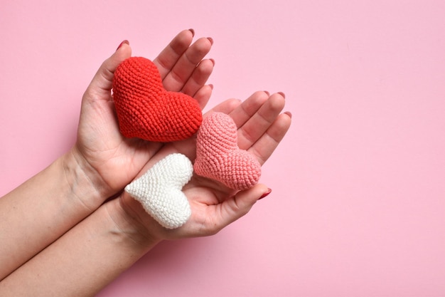 Knitted hearts in the hands of a girl with a beautiful manicure on a pink background Love Organ donation Pregnancy valentine's day Space for copying Flat position top view