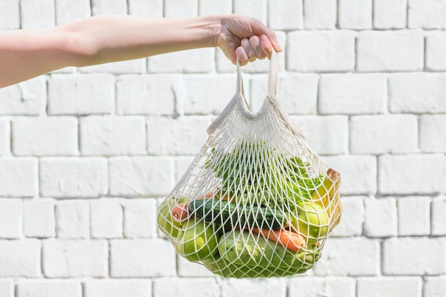 Knitted mesh bag with vegetables and fruits on the background of a white brick wall