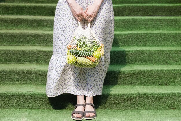 Knitted mesh bag with vegetables and fruits in the hands of a\
woman