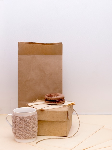 Вязаная кружка, картонная коробка и миндальное печенье с шоколадом на бумажном пакете