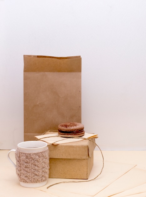 Photo knitted mug, cardboard box and chocolade macaroon on paper bag