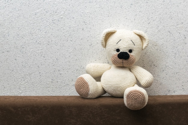 Knitted polar bear with brown paws on the sofa against the wall. Beautiful knitted toy.