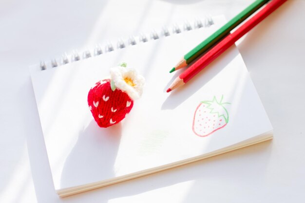 Photo a knitted strawberry is lying on the album painted berry with pencils handmade