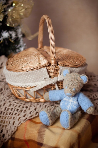 Knitted toy bear or mouse, in sweater sits near wicker basket and knitted plaid