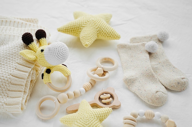 Knitted toy giraffe, yellow stars and wooden teether for newborn on white bed.  Gender neutral  baby stuff and accessories.