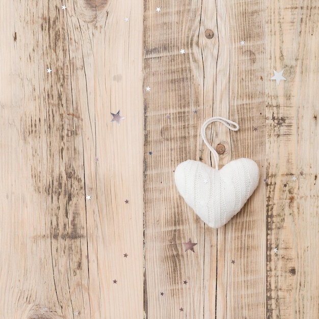 Knitted white heart Christmas decoration on retro wooden background with sparkling stars Holiday season and celebration concept