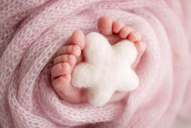 Knitted white star in the legs of a baby Soft feet of a new born in a pink wool blanket Closeup of toes heels and feet of a newborn Macro photography the tiny foot of a newborn baby