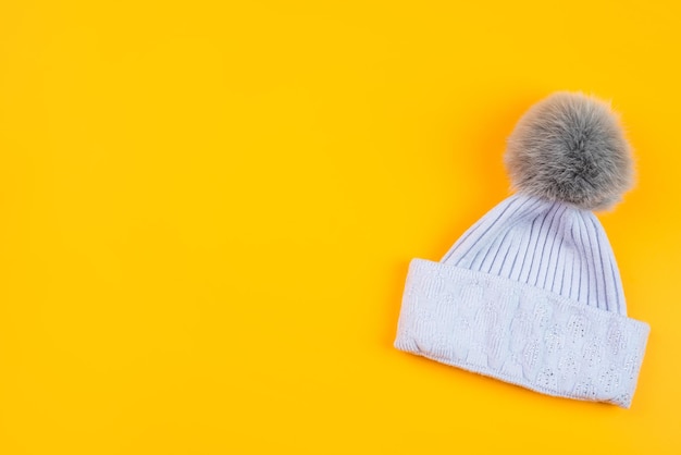 Knitted winter beanie hat on yellow background with copy space, fashion