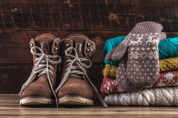 Knitted, winter, folded sweaters, warm mittens and winter boots on a wooden background. Winter clothes. Warm, comfortable clothes