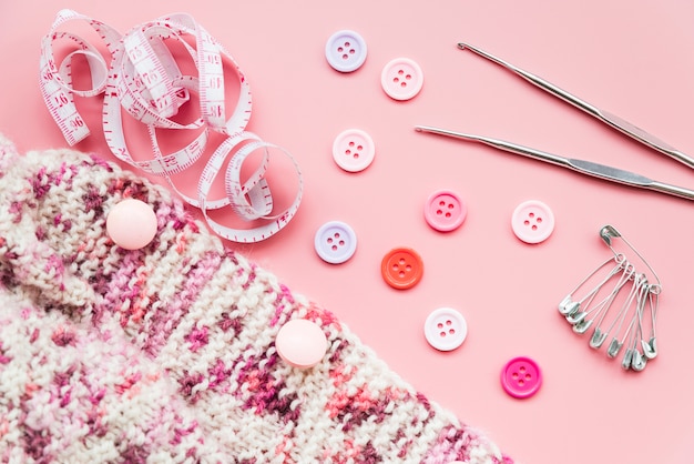 Knitting crochet; measuring tape; buttons; safety pins and needles on pink backdrop