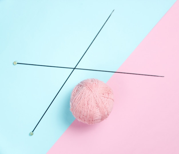 Knitting needles, skeins of wool on a pink-blue pastel background. Top view