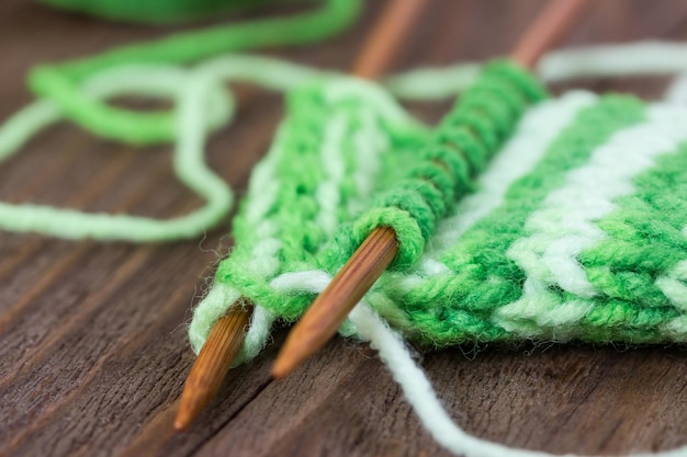 knitting pattern of green yarn on wooden needles and skein on a wooden background
