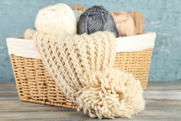 木製の背景に、バスケットでスカーフと毛糸を編む