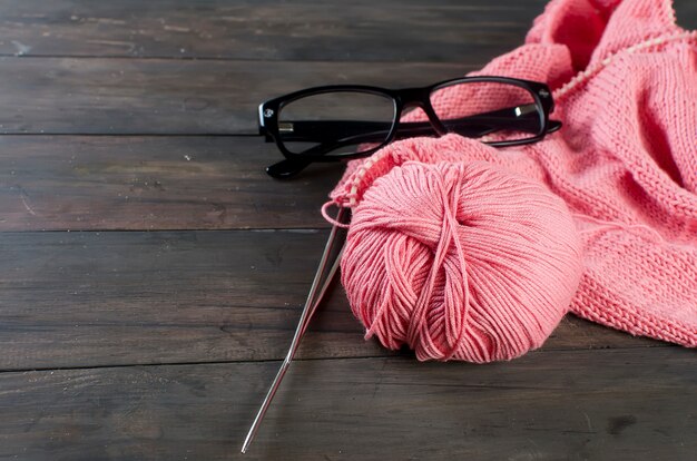Knitting threads and glasses on a wooden table.