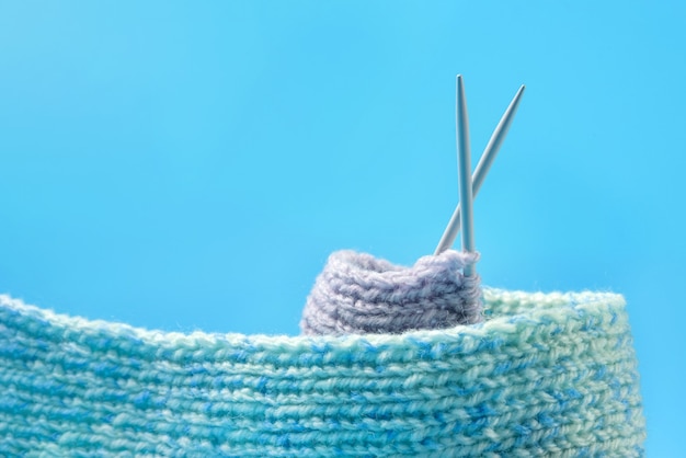 Knitting with crossed needles isolated on blue background with copy space. Passion for needlework.