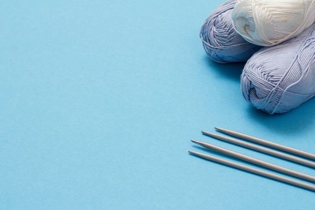 青の背景に毛糸のボールと金属の編み針を編みます。編み物のコンセプト。コピースペースのある上面図。