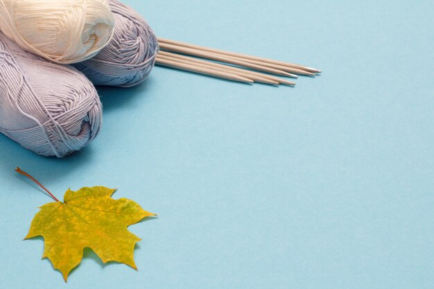 Knitting yarn balls, metal knitting needles and maple leaf on a blue background. Knitting concept. Top view.