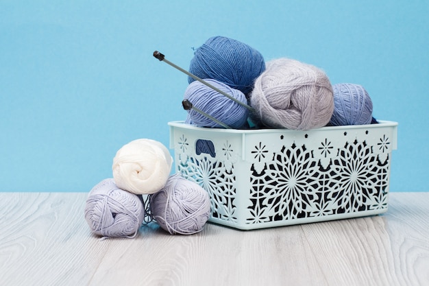 Knitting yarn balls and metal knitting needles in plastic\
basket on wooden boards and blue background. knitting concept.