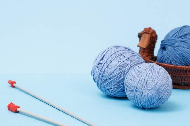 Knitting yarn balls, metal knitting needles and wicker basket on a blue background. Knitting concept.