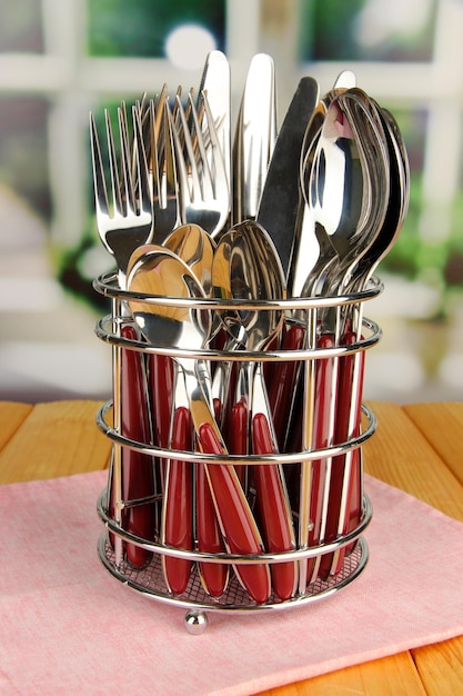 Knives forks and spoons in metal stand on table on bright background