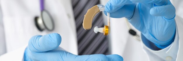 KNO-arts die gehoorapparaat vasthoudt met rubberen handschoenen close-up