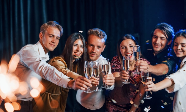 Knocking glasses. Group of cheerful friends celebrating new year indoors with drinks in hands.