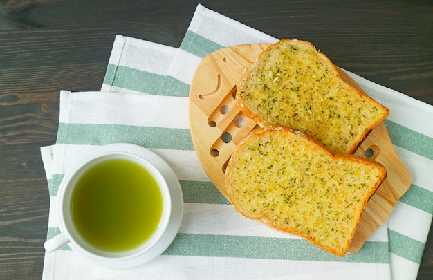 Knoflook boter Toasts op Breadboard met een kopje hete groene thee op zwarte houten tafel