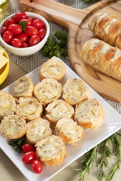 Knoflookbrood in witte vierkante plaat op tafel met kaas, rozemarijn, olijven en kerstomaatjes. Bovenaanzicht.