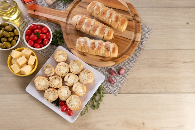 Knoflookbrood in witte vierkante plaat op tafel met kaas, rozemarijn, olijven en kerstomaatjes. Bovenaanzicht.