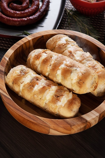 Knoflookbrood op een rode plaat op de barbecuetafel met worst, kaas, rozemarijn, olijven en kerstomaatjes.