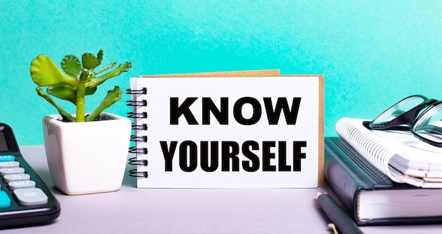 KNOW YOURSELF is written on a white card next to a potted flower, diaries and calculator. Organizational concept