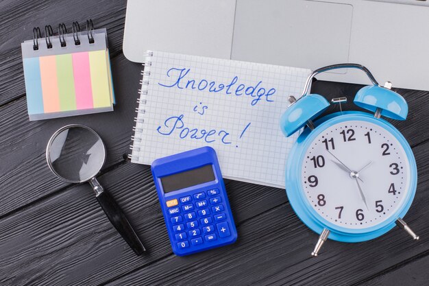 Knowledge is power. Alarm clock with calculator and glass magnifier on dark wooden table.