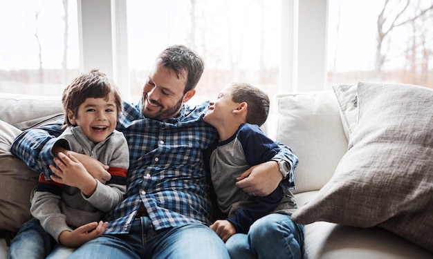 Knuffel gelukkig en portret van vader met kinderen op de bank voor liefdeszorg en ontspan in het ouderlijk huis Glimlach grappig en vader met jongenskinderen voor quality time genegenheid en komedie op de bank van een huis
