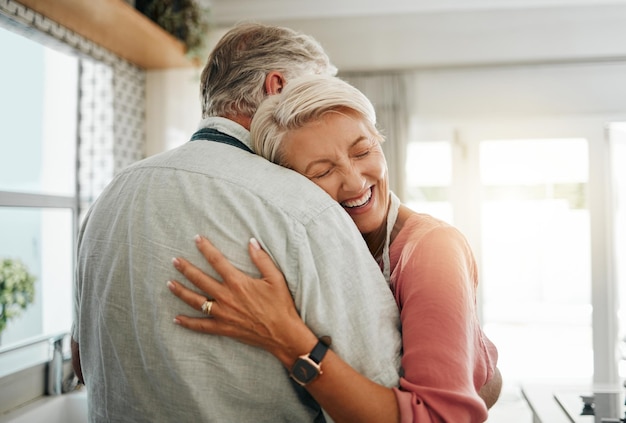 Knuffel liefde en veilig met een senior koppel dat samen knuffelt of omhelst in de keuken van hun huis Gelukkige glimlach en genegenheid met een oudere mannelijke en vrouwelijke gepensioneerde die een warme omhelzing deelt