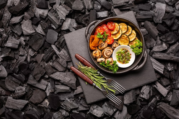 Koekenpan met barbecue groenten op een stenen snijplank op kolen. Bovenaanzicht.