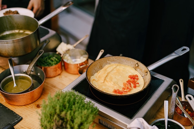 Koekenpan met een pannenkoek op het fornuis tijdens het koken in de keuken met metalen pollepels met voedsel