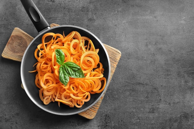 Koekenpan met rauwe wortelspaghetti op houten bord