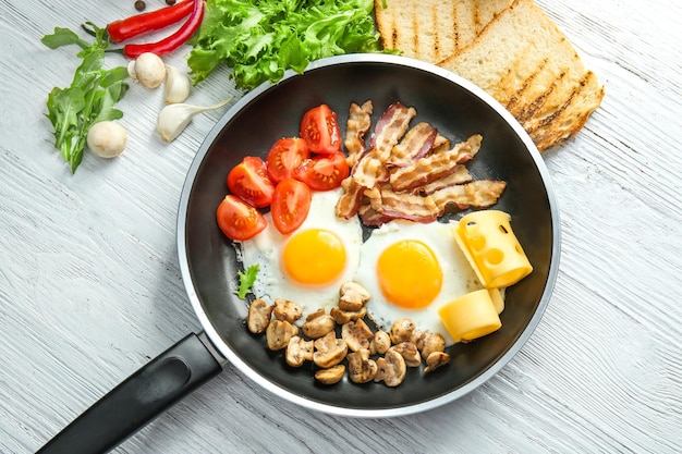 Koekenpan met smakelijke eieren, spek en champignons op tafel