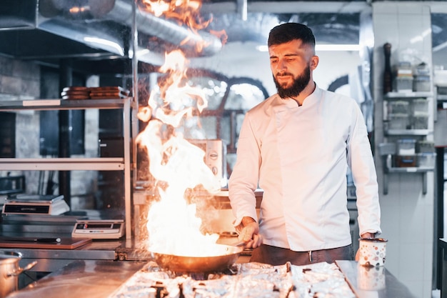 Koekenpan staat in brand Chef-kok in wit uniform kookt eten in de keuken Drukke dag op het werk