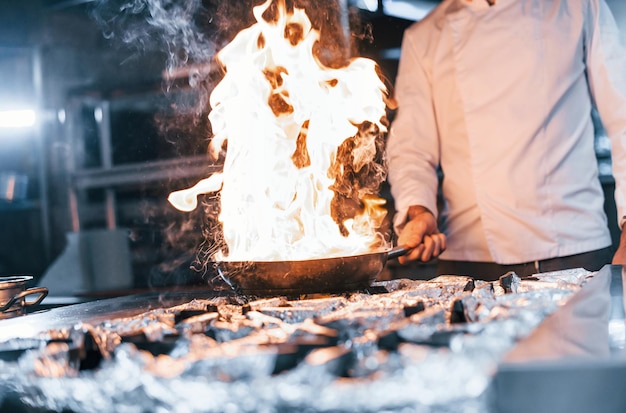 Koekenpan staat in brand Chef-kok in wit uniform kookt eten in de keuken Drukke dag op het werk