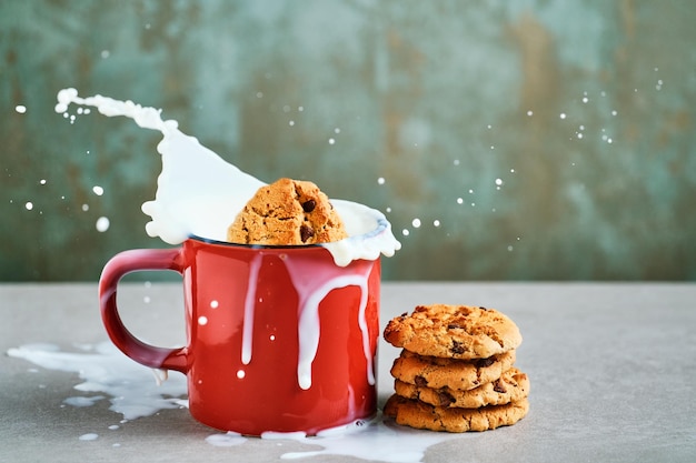 Koekje met stukjes chocolade vallen in een rode mok gevuld met opspattende melk