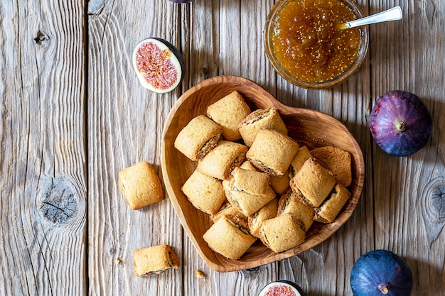 Koekjes gevuld met vijgenjam op houten kom, verse vijgen, jam in pot op houten ondergrond. Bovenaanzicht