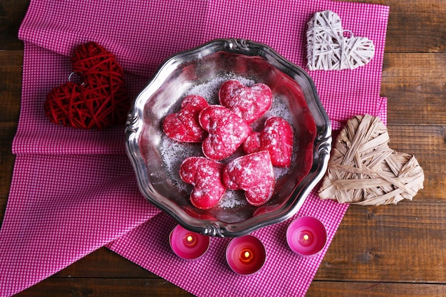 Koekjes in de vorm van een hart op een metalen dienblad met kaarsen en servetten op een rustieke houten tafelachtergrond