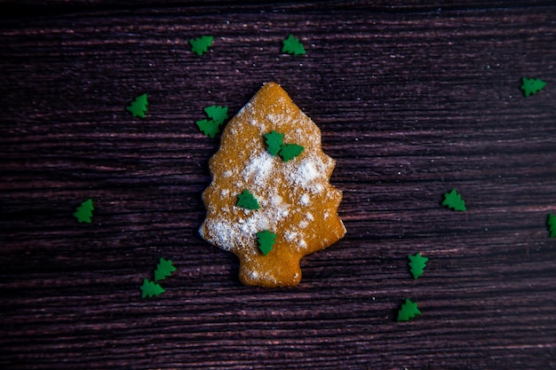 Koekjes in de vorm van een kerstboom gestrooid op witte bloem en kleine groene kerstt...